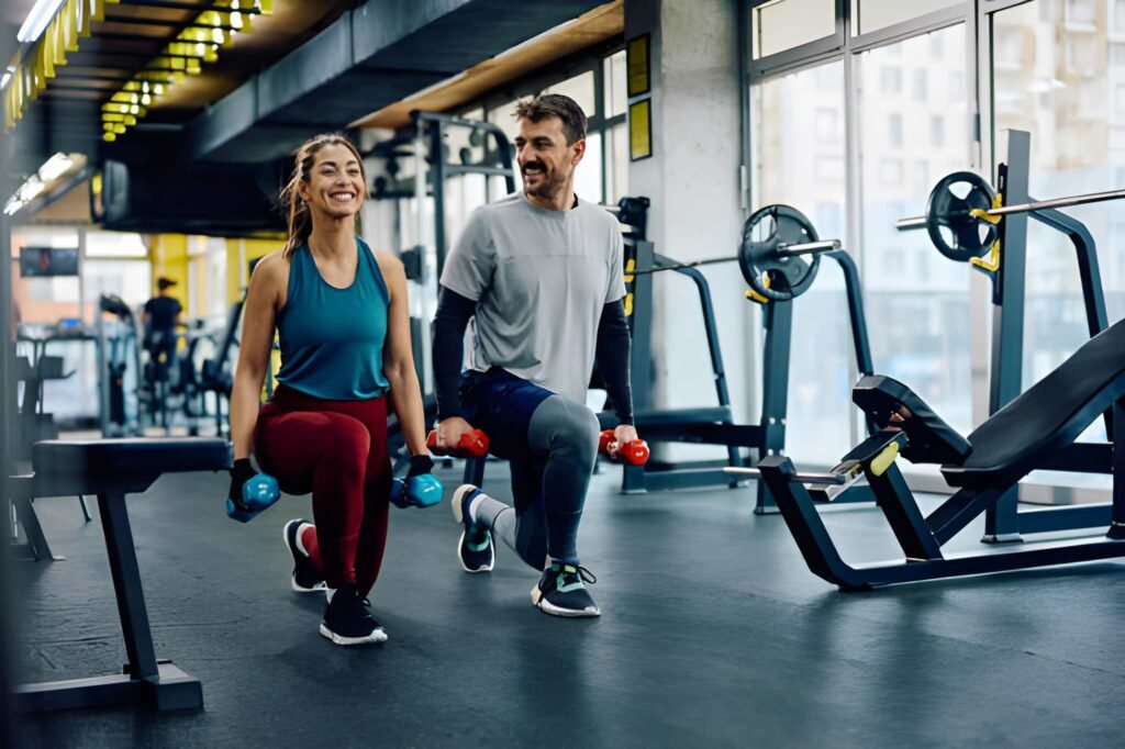 Happy athletic couple exercising with hand weights in lunge position in a gym.